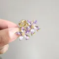 Gros plan d'une petite pince à cheveux dorée avec deux fleurs en cristal violet en main - Style Fleur en Cristal Marquise (ZJ007 Pourpre Lotus) / Pourpre Lotus (ZJ007 Pourpre Lotus)