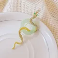Spilla a serpente dorata con cristalli, anello verde e perla su vassoio in ceramica bianca - Oro