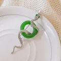Dettaglio ravvicinato di una spilla a serpente argento con cristalli, perla e anello verde - Argento