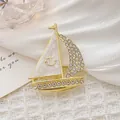 Detailweergave van een gouden zeilbootbroche met emaille en strass accenten - Zeilboot vorm / Goud