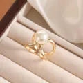 Close-up of a golden crisscross ring with a large white pearl in a beige jewelry box - Gold Intertwined Line Style