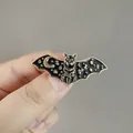 Handgehaltene Ansicht einer schwarzen Fledermausbrosche mit goldenen Sternen und Mond - Emaille Stern Mond Fledermaus Stil