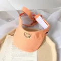 Light orange open-top sun visor for kids featuring a stitched smiley face and adjustable strap - One Size / Orange