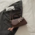 Elegante braune Lederhandtasche mit goldener V-Schnalle auf grauem Designer-Anzug - Braun