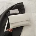 Close-up of white envelope clutch bag with wrist strap against a grey blazer backdrop - White