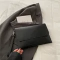 Close-up of a minimalist black envelope clutch bag on a grey suit with a modern book - Black