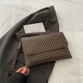 Détail d'une pochette enveloppe marron avec monogramme portée avec un blazer gris chic - Monogramme Café