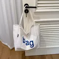 Witte canvas draagtas met blauwe bag letters hangend aan een deurklink in een huiselijke setting - Wit