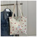 Dettaglio della borsa tote in tela crema con stampa a ciliegie rosse e trama intrecciata - Bianco