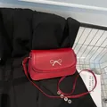 Bolso bandolera rojo con cierre de lazo dorado sobre blazer negro para un look de moda - Rojo