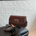 Minimalist dark brown leather crossbody bag with a delicate gold bow buckle detail - Brown