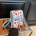 Light blue crossbody bag featuring red strawberry print and golden charm details - Strawberry Blue