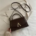 Dunkelbraune kleine Ledertasche mit goldener V-Schließe auf beigem Blazer - Braun