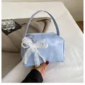 Close-up of light blue handbag with lace bow and pearl charm detail and metal zipper - With Ornament / Blue