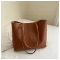 Detail view of brown faux leather tote bag with vertical stitching on white bedding - Brown