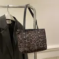 Detail of leopard print tote bag featuring black leather handles and gold rivet accents - Black