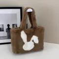 Detail of a brown plush tote bag with a white rabbit silhouette on a display stand - Khaki