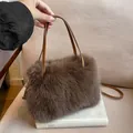 Schicke dunkelbraune Plüsch-Schultertasche mit hellbraunem Ledergriff auf weißem Buch - Braun