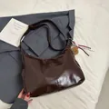 Dunkelbraune glänzende Lackleder-Hobo-Tasche mit süßem Bärenanhänger auf neutralem Grund - Braun