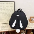 Mochila escolar negra con orejas de conejo blancas y pompón sobre mesa madera - Negro