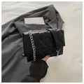 Detail of black quilted shoulder bag with silver chain strap on a grey blazer - Black