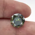 Donkergroene briljant geslepen moissaniet edelsteen tussen vingers op witte achtergrond - 5mm / Teal
