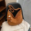 Bolso grande de pana marrón tipo hobo con parche deportivo y peluche sobre un sillón - Marrón (Con Colgante)