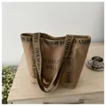 Détail du sac cabas en toile kaki avec imprimé lettres noires sur une surface en bois - Marron