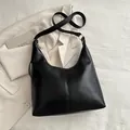 Glossy black hobo shoulder bag with gold metal rings on a white textured backdrop - Black
