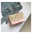 Rosa Stroh-Eimertasche mit Erdbeerstickerei und Lederriemen vor Jeans-Hintergrund - Rosa