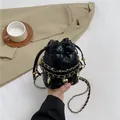 Mini-Eimerbeutel in Schwarz mit Steppmuster, Goldkette und Herzanhängern am Tisch - Schwarz