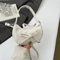 Creamy white crescent handbag featuring bow detail and silver beads in hand view - White