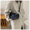 Nahaufnahme einer schwarzen matten Satteltasche mit Goldschnalle auf cremefarbenem Mantel - Schwarz