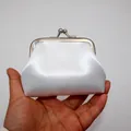 Dettaglio di un mini portamonete in raso bianco con chiusura a scatto tenuto in mano - Bianco / 3 Pollici