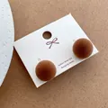 Close-up of plush ball stud earrings with 925 silver needles on a decorative background - Dark Coffee