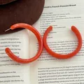 Details von bernsteinbraunen Harz-Creolen in C-Form auf Buch und Filzhut - C-förmiger Marmormuster-Stil (F-19) / Orange