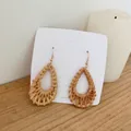 Close-up of handmade teardrop-shaped woven rattan earrings with bohemian golden hooks - Teardrop Rattan Woven