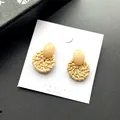 Detail van gevlochten rotan oorbellen met roze hars studs op witte sieraden display kaart - Beige Licht Rotan