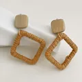 Dettaglio di orecchini quadrati in rafia intrecciata con perno in legno naturale e oro - Legno Naturale Chiaro - Stile Quadrato in Raffia Cammello (A288)