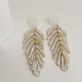 Macro detail of cascading white leaf acrylic earrings with golden chain links and pearl sheen - White
