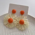 Detail van handgemaakte raffia madeliefjes oorbellen met oranje kralen en witte bloemen - Beige/Oranje