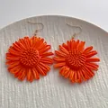 Handgefertigte orangefarbene Raffia-Blumenohrringe im Boho-Stil auf weißem Teller - Orange