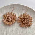 Macro view of handmade raffia sunflower earrings with golden hooks on white ceramic - Brown