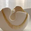 Elegante gouden franje halsketting op een getextureerde keramische schaal met minimalistisch design - Goud