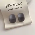 Gros plan de boucles d'oreilles carrées en résine gris foncé sur ruban beige - Bleu Brume