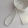 Détail d'un élégant collier de perles blanches avec fermoir argenté sur un plat en céramique - Collier de perles 8mm