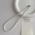 Vue détaillée de perles blanches rondes avec un fermoir mousqueton argenté sur plateau - Collier de perles 6mm