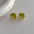 Dettaglio degli orecchini irregolari in resina verde e metallo dorato su sfondo materico - Verde