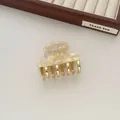 Macro shot of a cream pearl textured hair claw clip with gold-plated metal teeth on beige surface - Fairy White