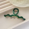 Macro shot of dark green acetate hair claw clip with elegant gold spring and wavy texture - Vintage Green